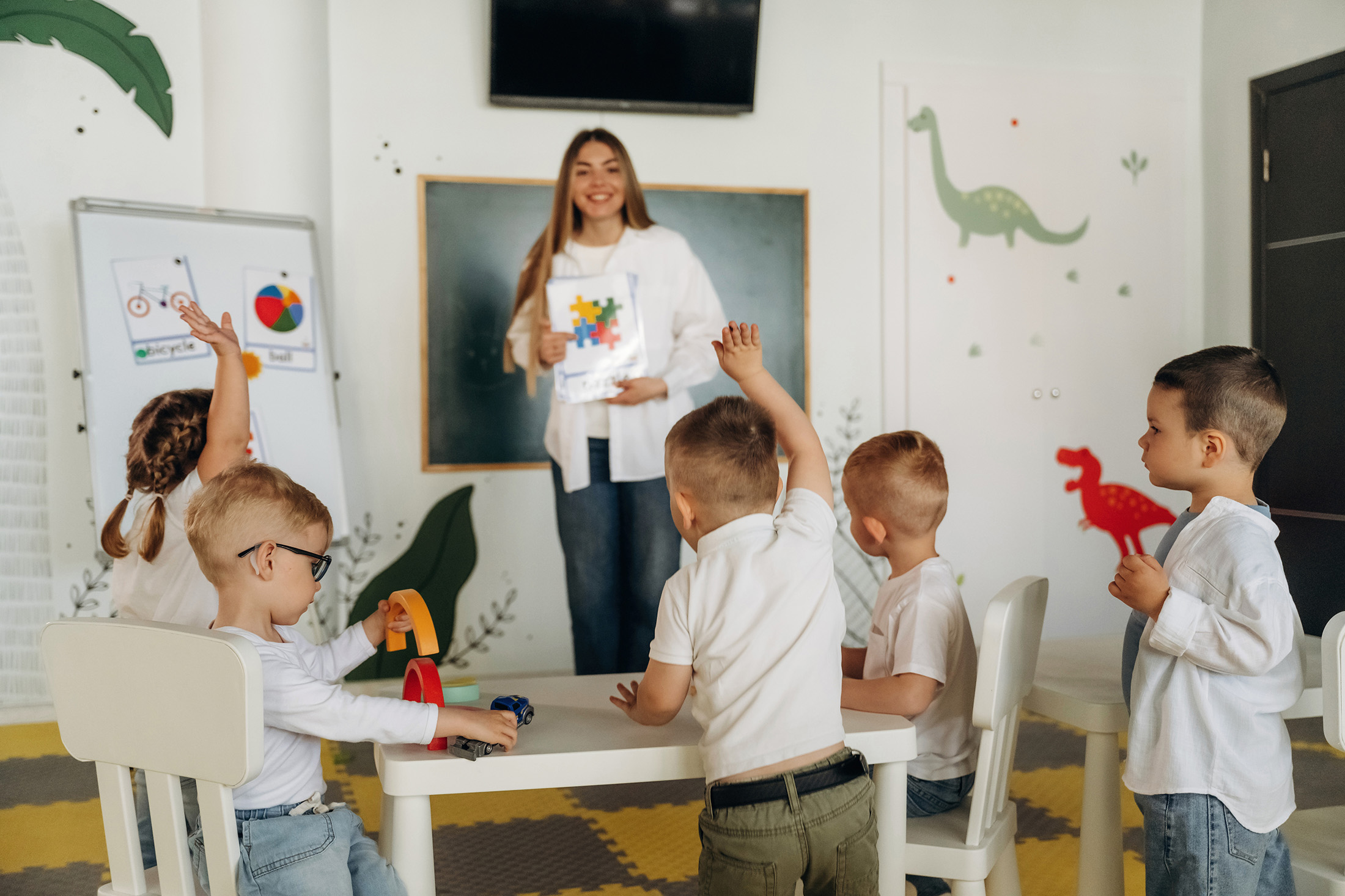 Female is standing and showing picture of puzzle. Children in kindergarten with their teacher.