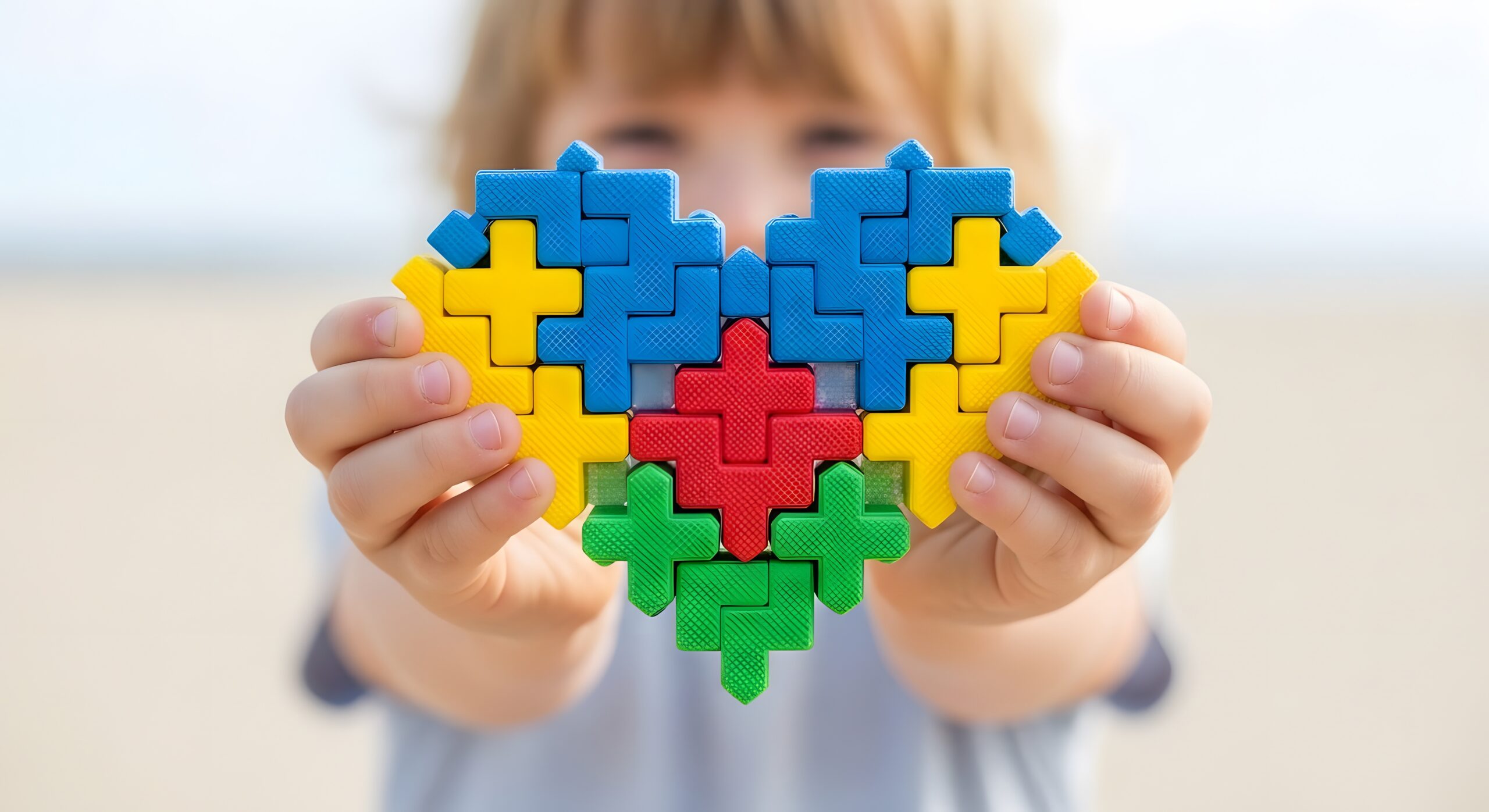 Child holds a colorful puzzle heart symbol for autism awareness with awareness