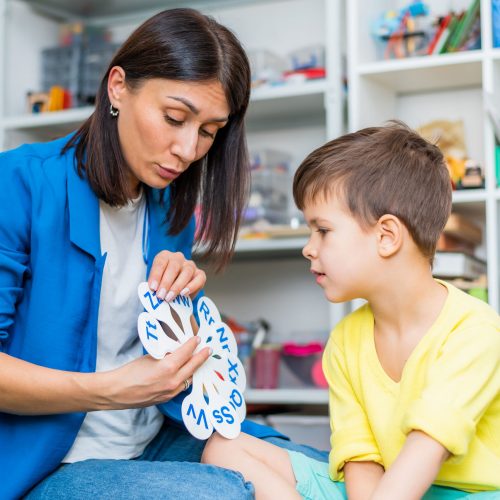 A cute child with a speech therapist is taught to pronounce the letters, words and sounds correctly.